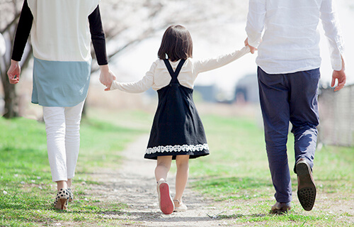 親子が３人で手を繋いで晴れた芝生を歩いている様子